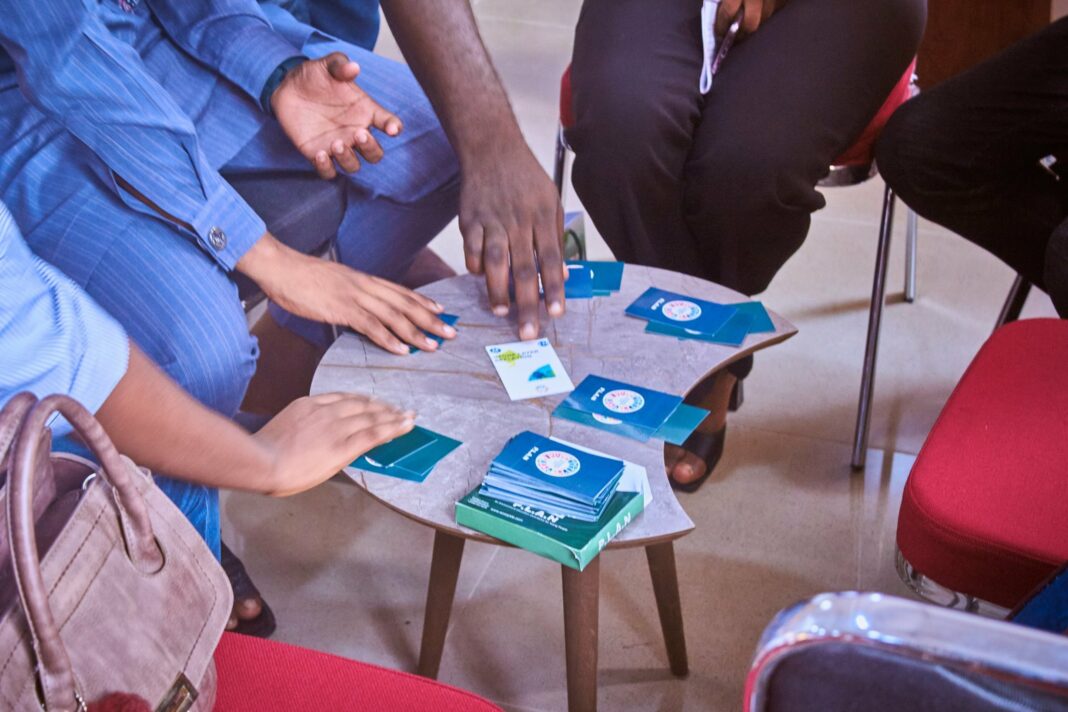 A group plays PLAN card game at a small central table.